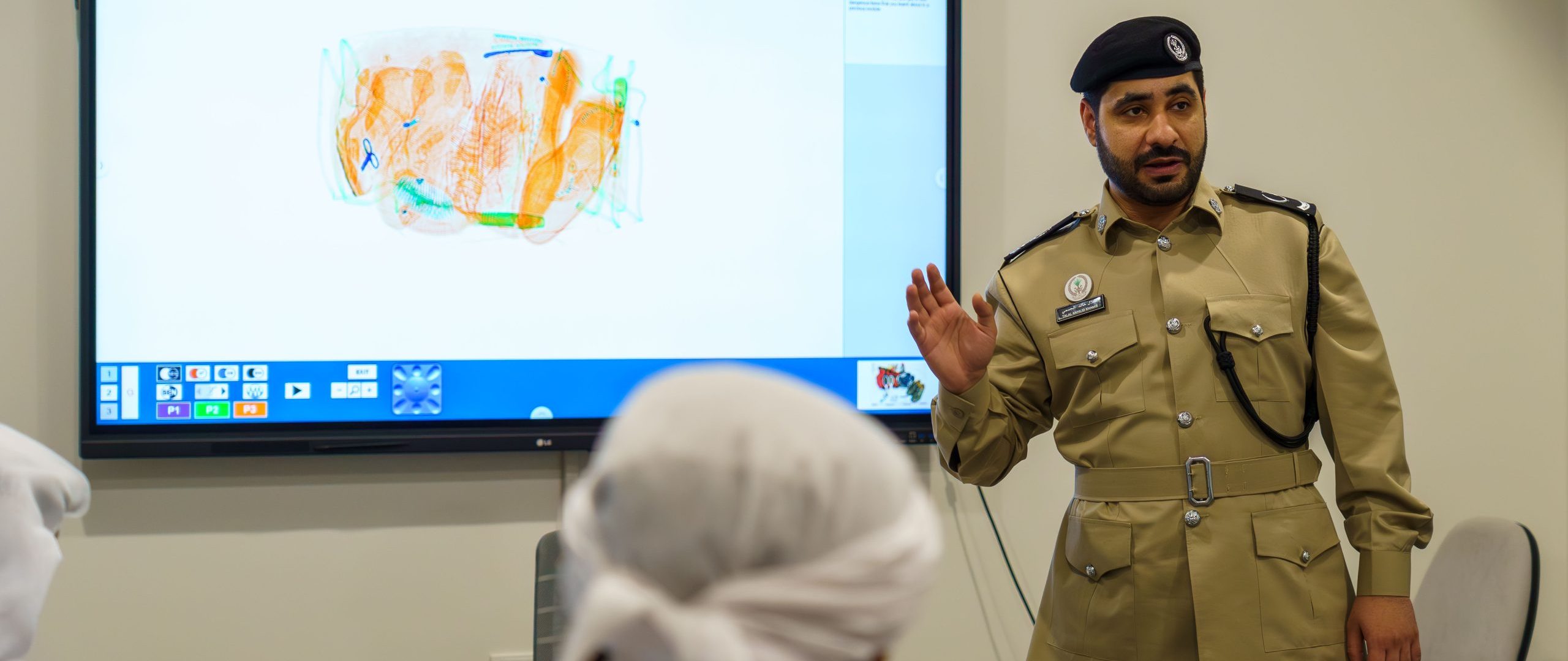 Man in military uniform in front of a screen showing x-rayed baggage.
